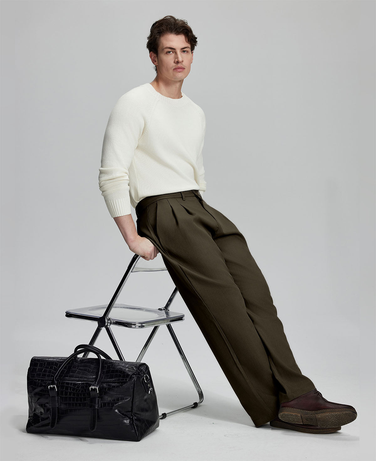 Styled with white sweater and black bag, leaning on chair¡ªelegant yet relaxed look in men¡¯s coffee baggy pleated dress pants.