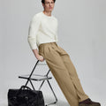 Styled with white sweater and black bag, leaning on chair¡ªelegant yet relaxed look in men¡¯s khaki baggy pleated dress pants.