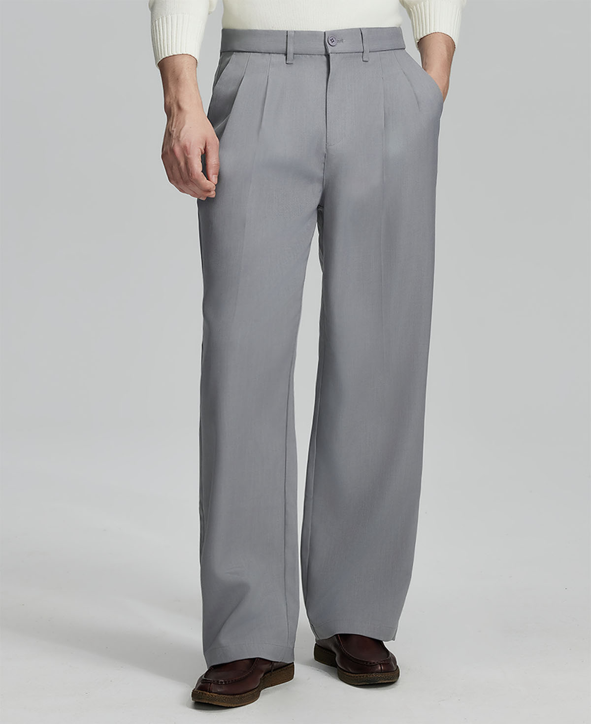 Man in white knit, light grey wide-leg dress pants and brown shoes¡ªhand in pocket showing pleated front and fluid drape.