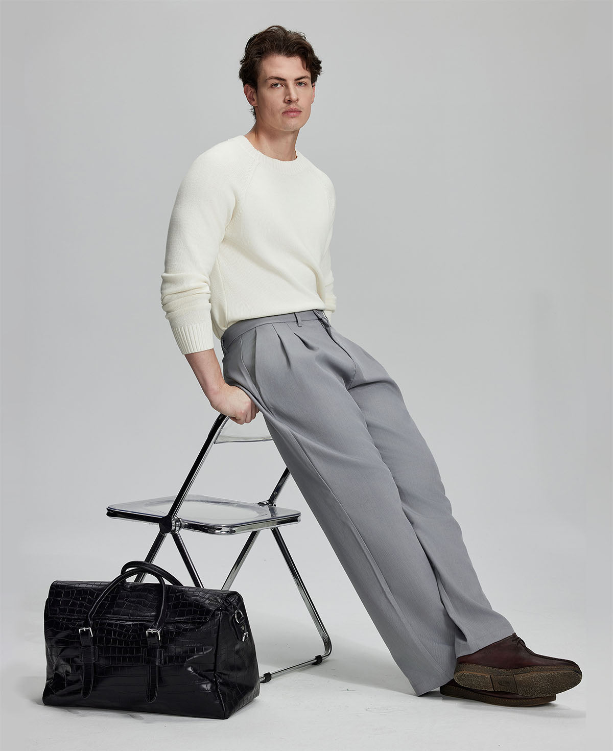 Styled with white sweater and black bag, leaning on chair¡ªelegant yet relaxed look in men¡¯s light grey baggy pleated dress pants.