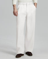Man in white knit, white wide-leg dress pants and brown shoes¡ªhand in pocket showing pleated front and fluid drape.