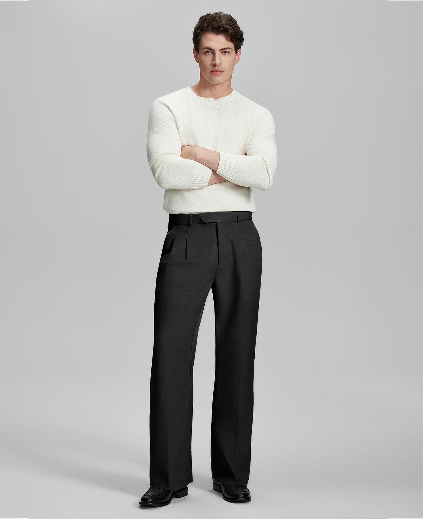 Model in white sweater, black trousers & black shoes, arms crossed, presenting a smart-casual style with Baggy Pleated Dress Pants for Men.