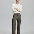 Model in white sweater, brown trousers & black shoes, arms crossed, presenting a smart-casual style with Baggy Pleated Dress Pants for Men.