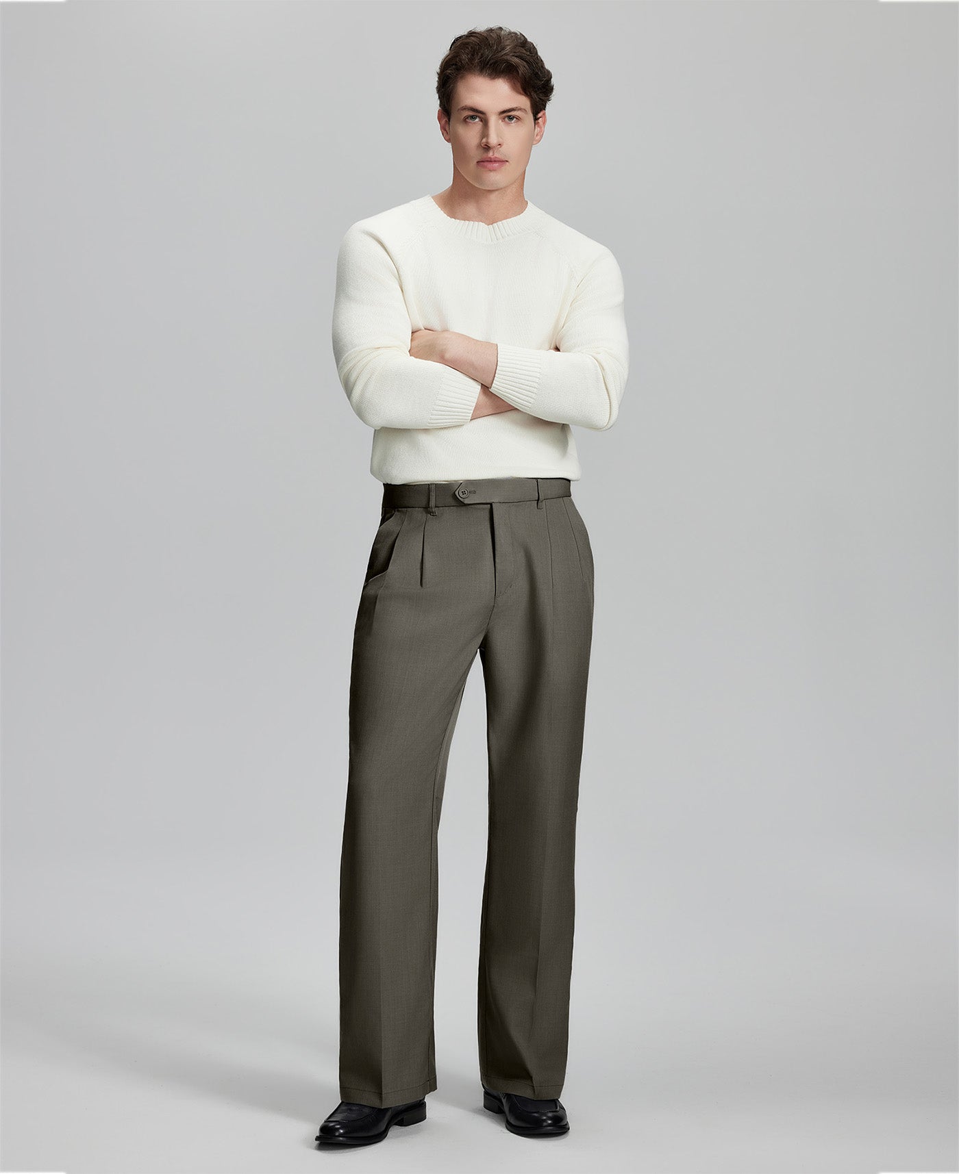 Model in white sweater, brown trousers & black shoes, arms crossed, presenting a smart-casual style with Baggy Pleated Dress Pants for Men.