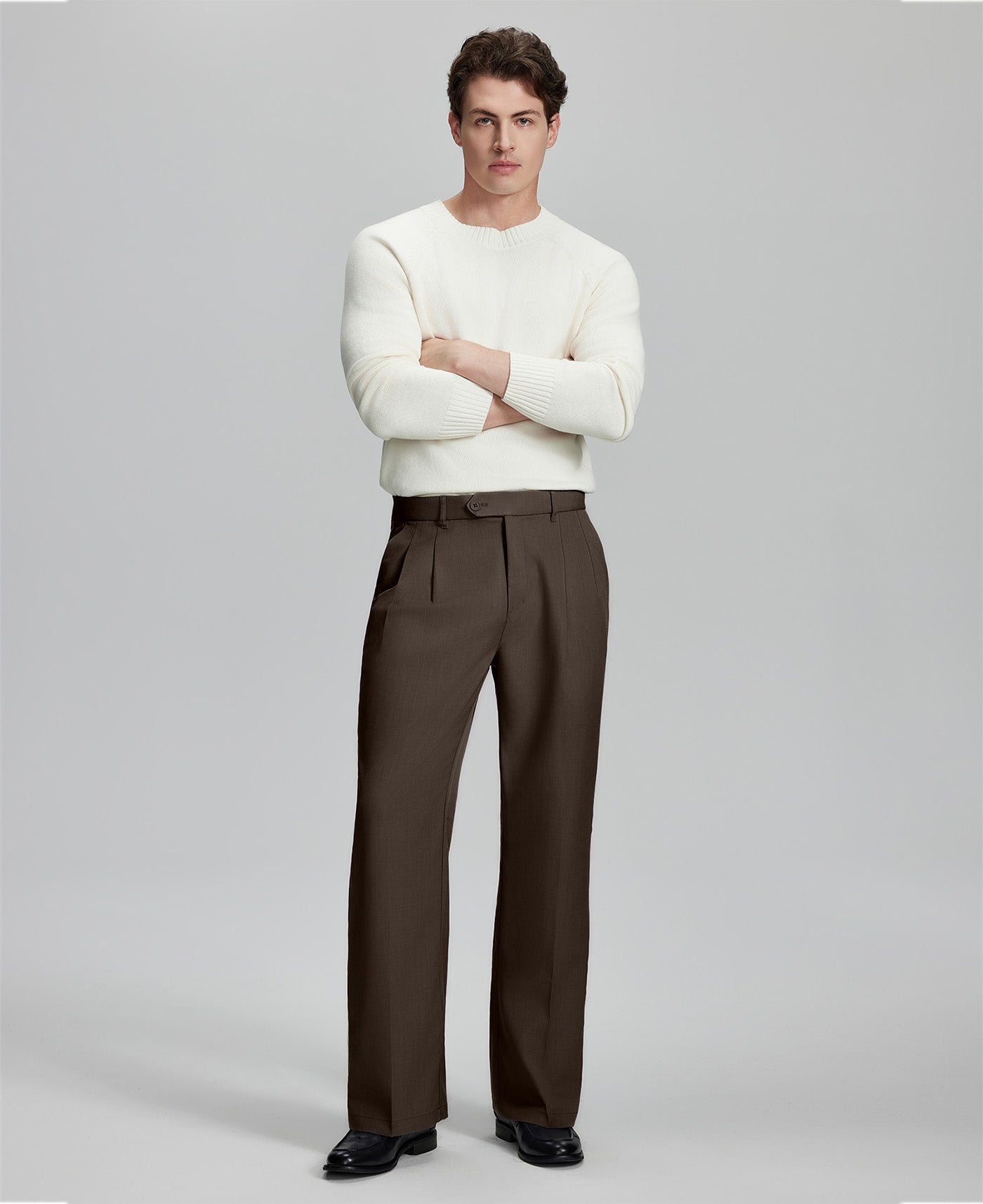 Model in white sweater, coffee trousers & black shoes, arms crossed, presenting a smart-casual style with Baggy Pleated Dress Pants for Men.