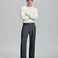 Model in white sweater, dark grey trousers & black shoes, arms crossed, presenting a smart-casual style with Baggy Pleated Dress Pants for Men.