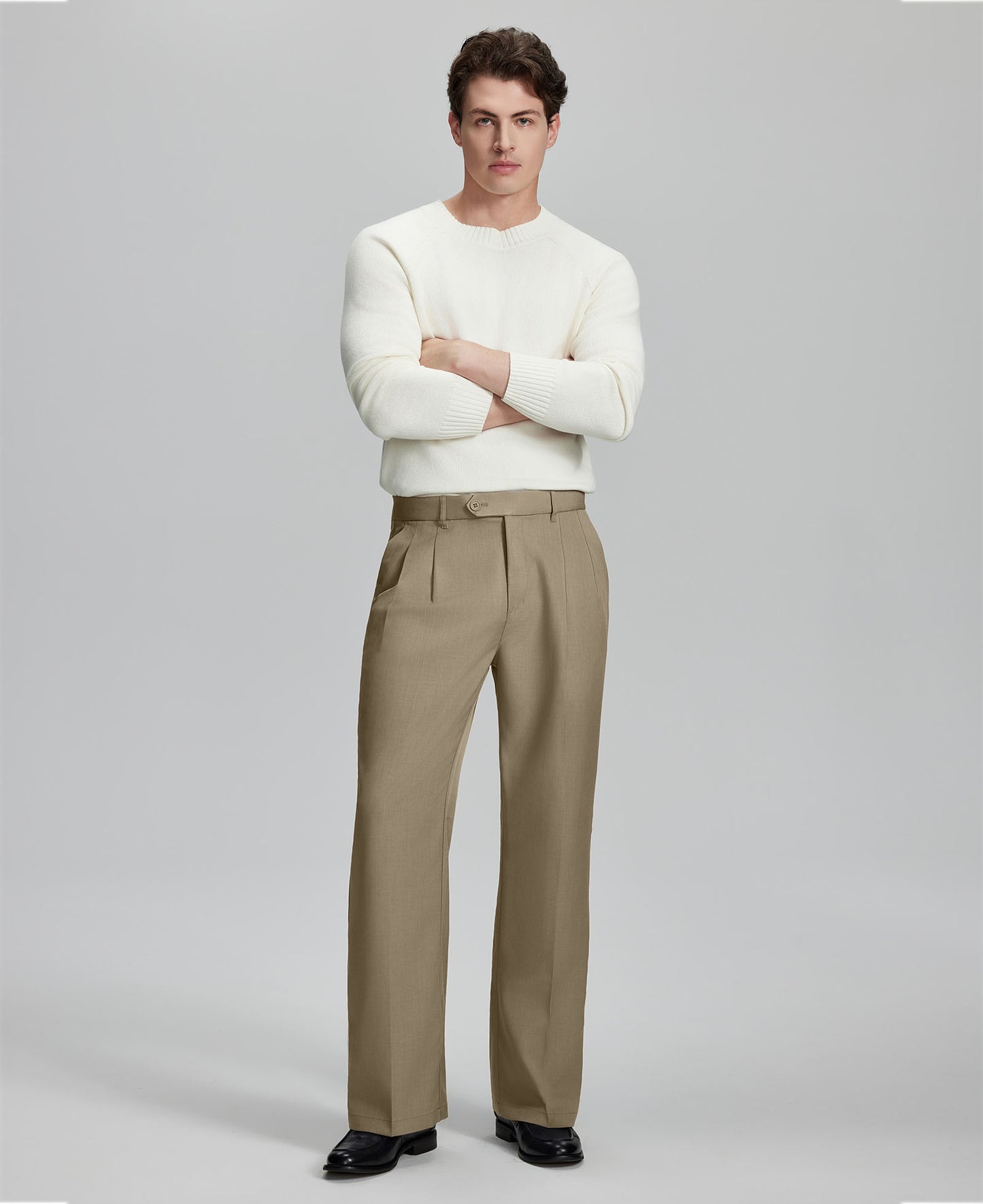 Model in white sweater, khaki trousers & black shoes, arms crossed, presenting a smart-casual style with Baggy Pleated Dress Pants for Men.