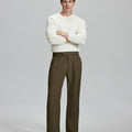 Model in white sweater, light brown trousers & black shoes, arms crossed, presenting a smart-casual style with Baggy Pleated Dress Pants for Men.