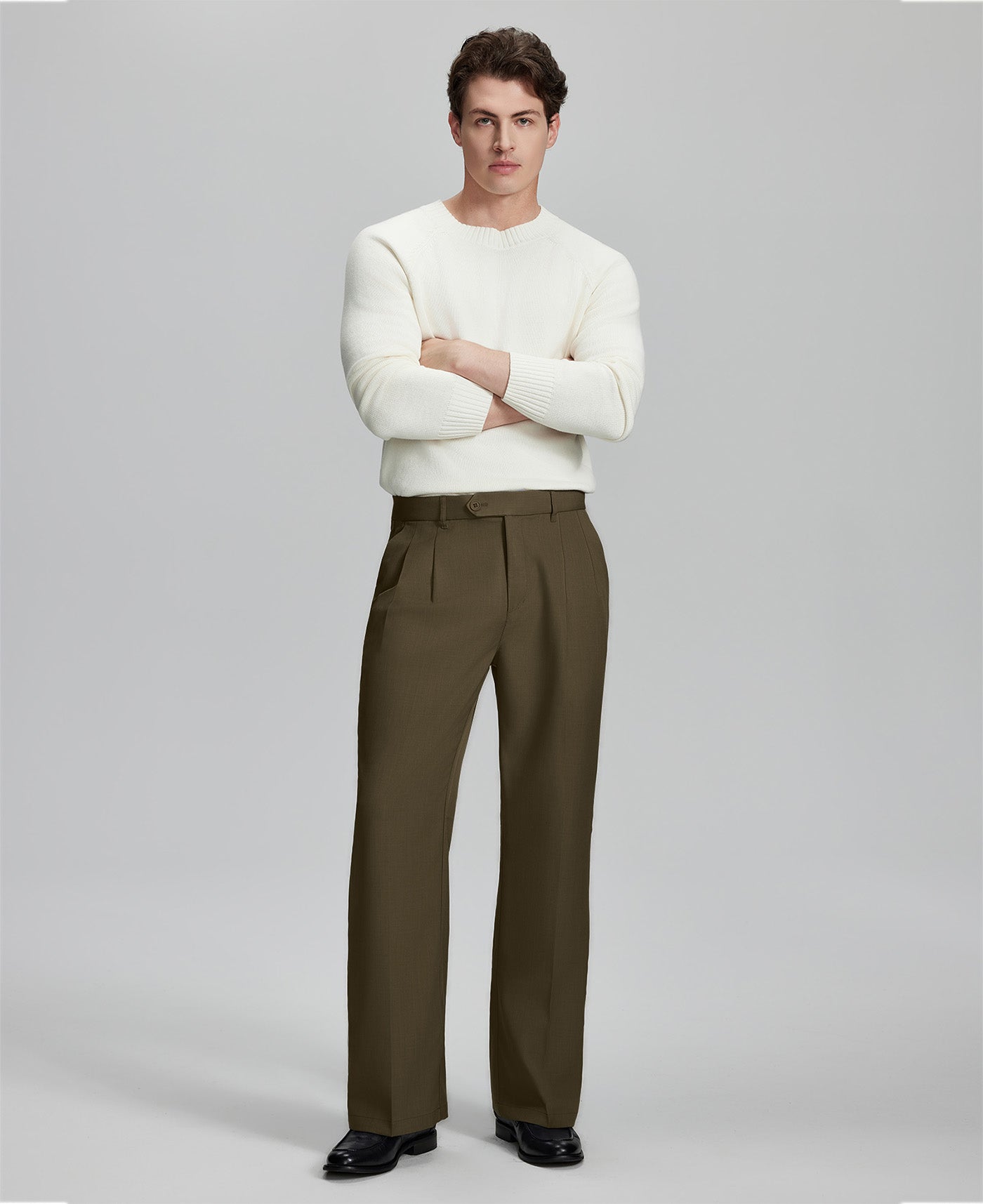 Model in white sweater, light brown trousers & black shoes, arms crossed, presenting a smart-casual style with Baggy Pleated Dress Pants for Men.