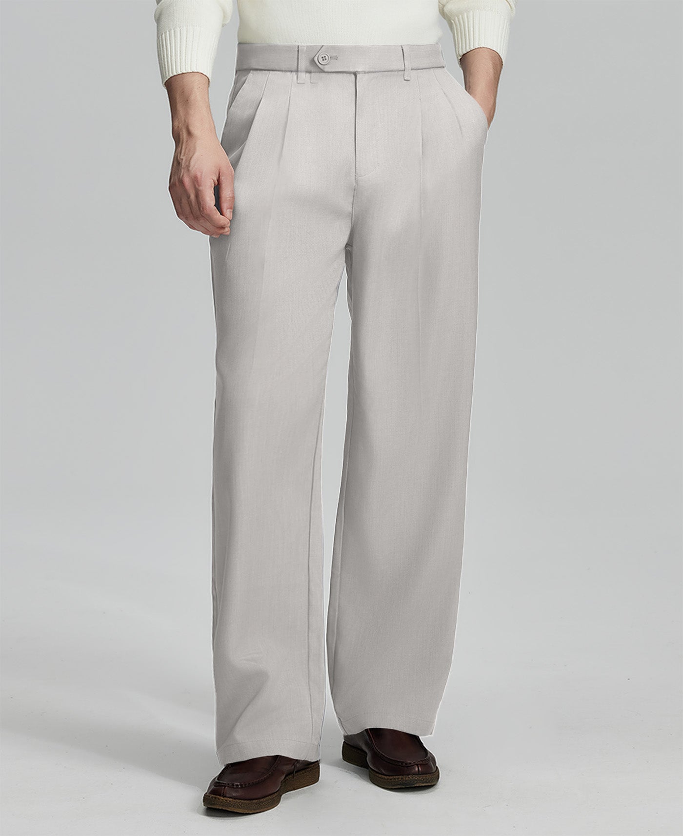 Man in white sweater, stone grey pleated pants & brown shoes, showcasing the wide-leg cut and drape of Baggy Pleated Dress Pants for Men.