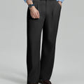 Man in light blue shirt, black pleated pants, and brown shoes, hand in pocket showcasing relaxed fit and drape.