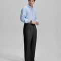 Side view of man adjusting cuff while highlighting the clean lines and casual elegance of black pleated baggy dress pants.