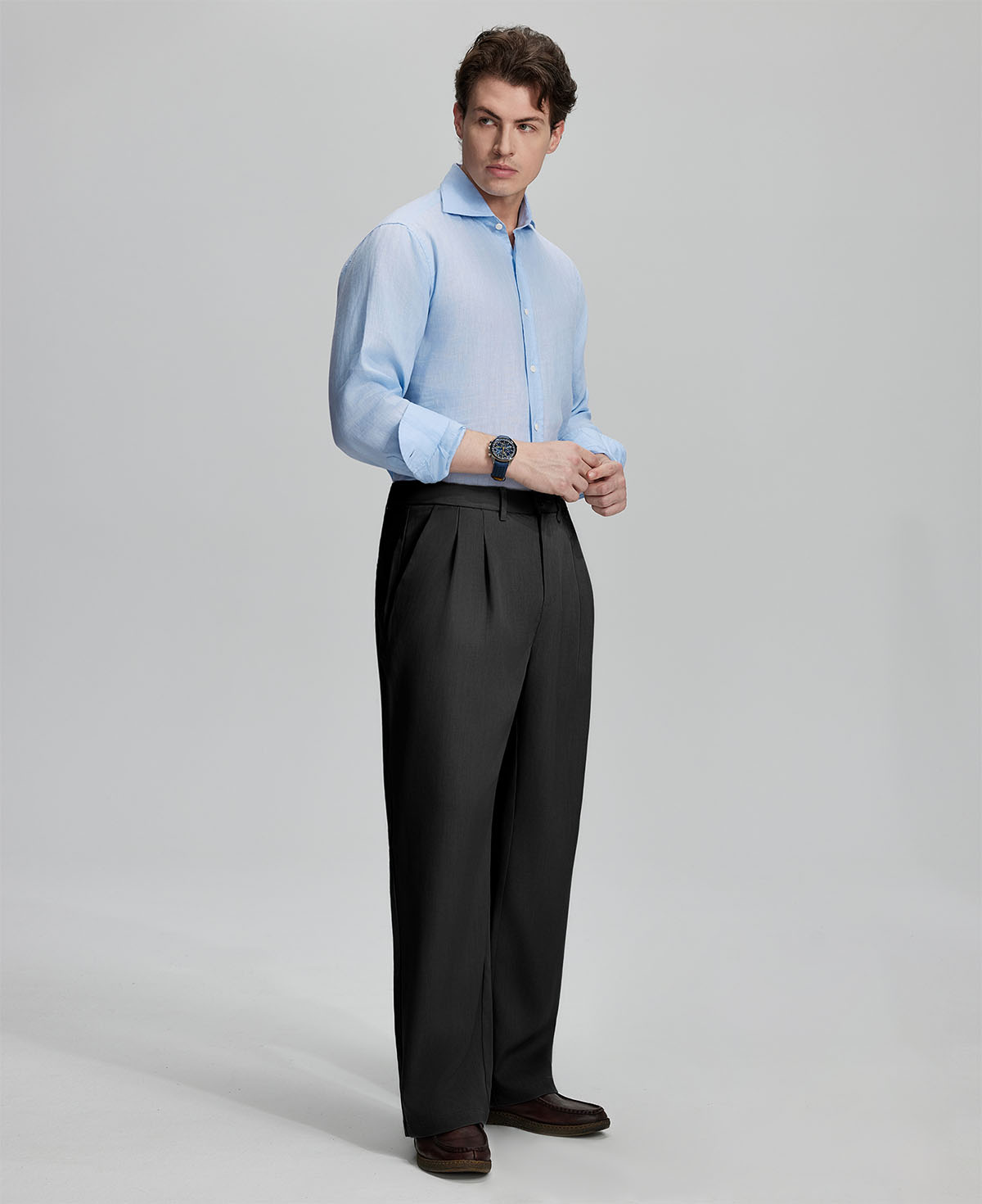 Side view of man adjusting cuff while highlighting the clean lines and casual elegance of black pleated baggy dress pants.