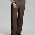 Man in light blue shirt, coffee pleated pants, and brown shoes, hand in pocket showcasing relaxed fit and drape.