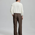 Side view of man adjusting cuff while highlighting the clean lines and casual elegance of coffee pleated baggy dress pants.