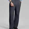 Man in light blue shirt, dark gray pleated pants, and brown shoes, hand in pocket showcasing relaxed fit and drape.