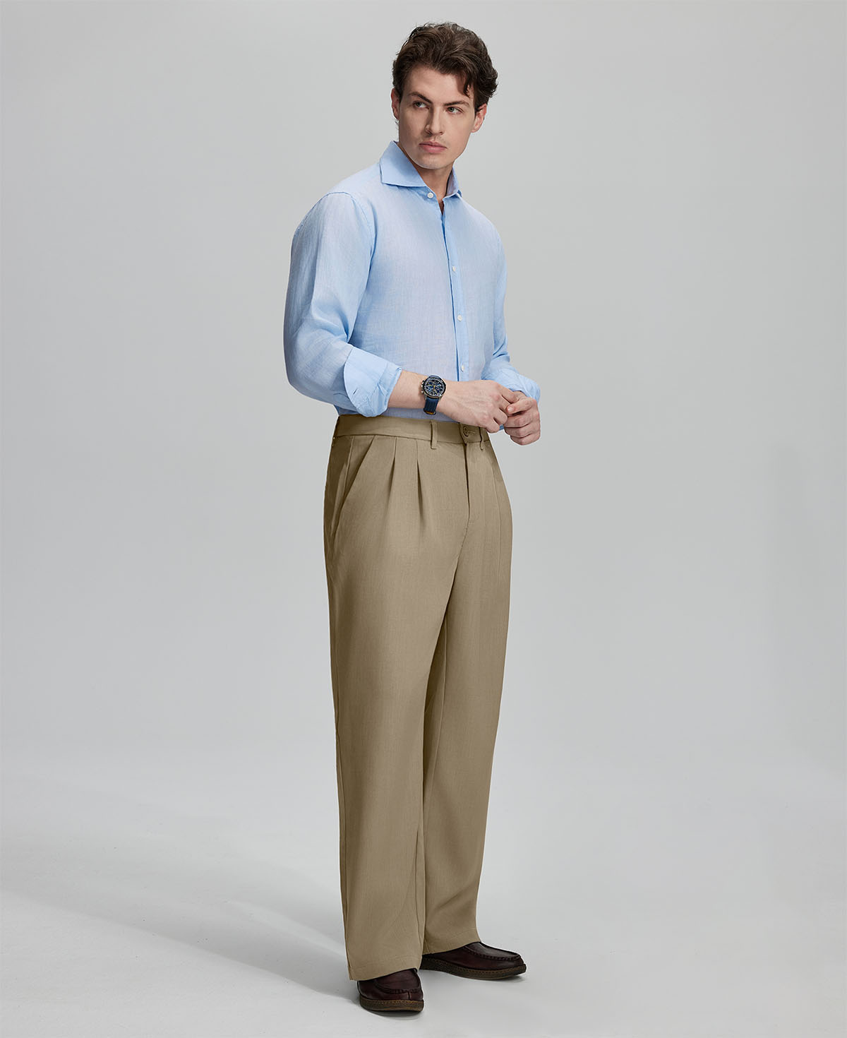 Side view of man adjusting cuff while highlighting the clean lines and casual elegance of khaki pleated baggy dress pants.