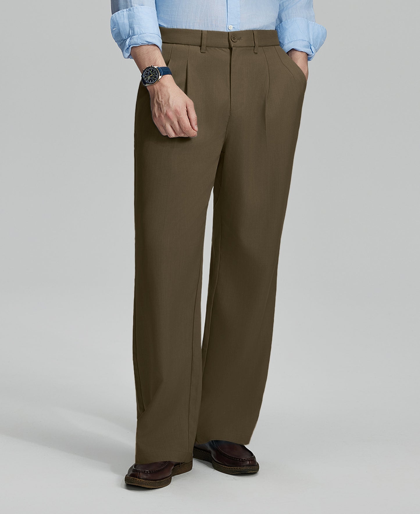 Man in light blue shirt, light brown pleated pants, and brown shoes, hand in pocket showcasing relaxed fit and drape.