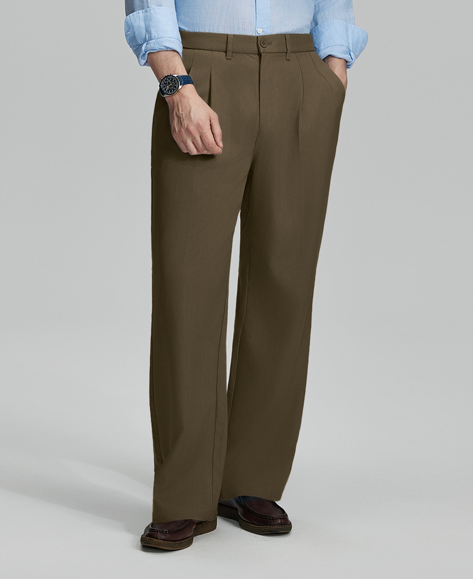 Man in light blue shirt, light brown pleated pants, and brown shoes, hand in pocket showcasing relaxed fit and drape.