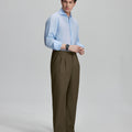 Side view of man adjusting cuff while highlighting the clean lines and casual elegance of light brown pleated baggy dress pants.