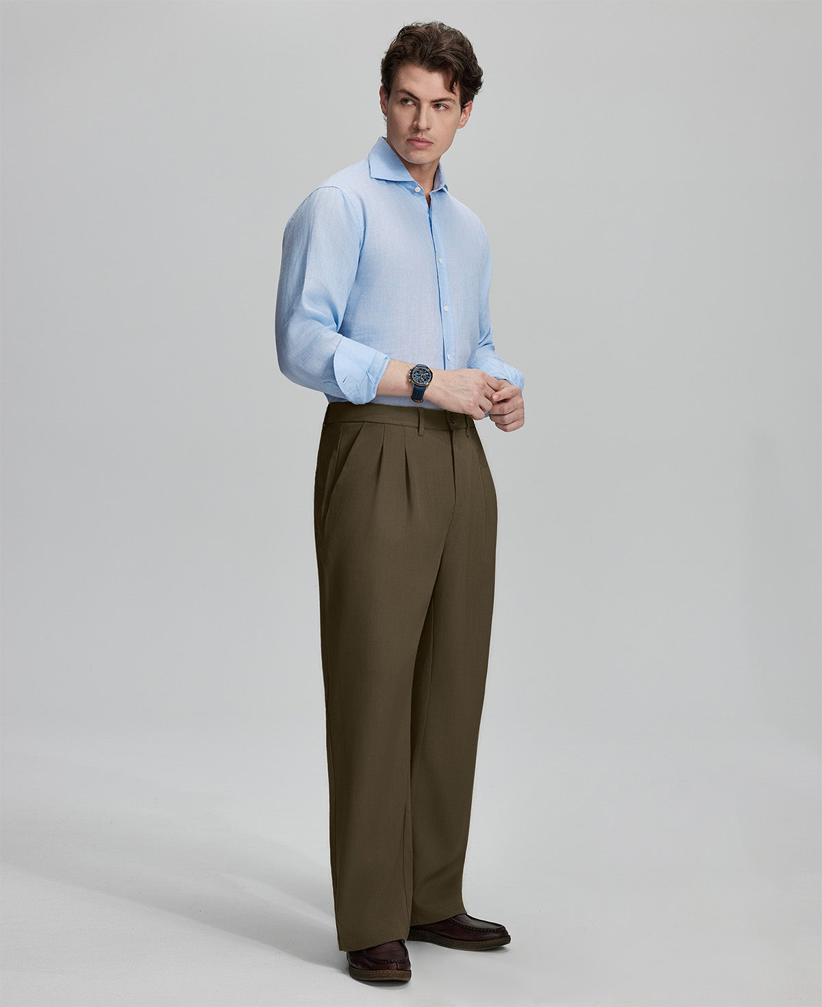 Side view of man adjusting cuff while highlighting the clean lines and casual elegance of light brown pleated baggy dress pants.