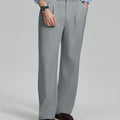 Man in light blue shirt, light grey pleated pants, and brown shoes, hand in pocket showcasing relaxed fit and drape.
