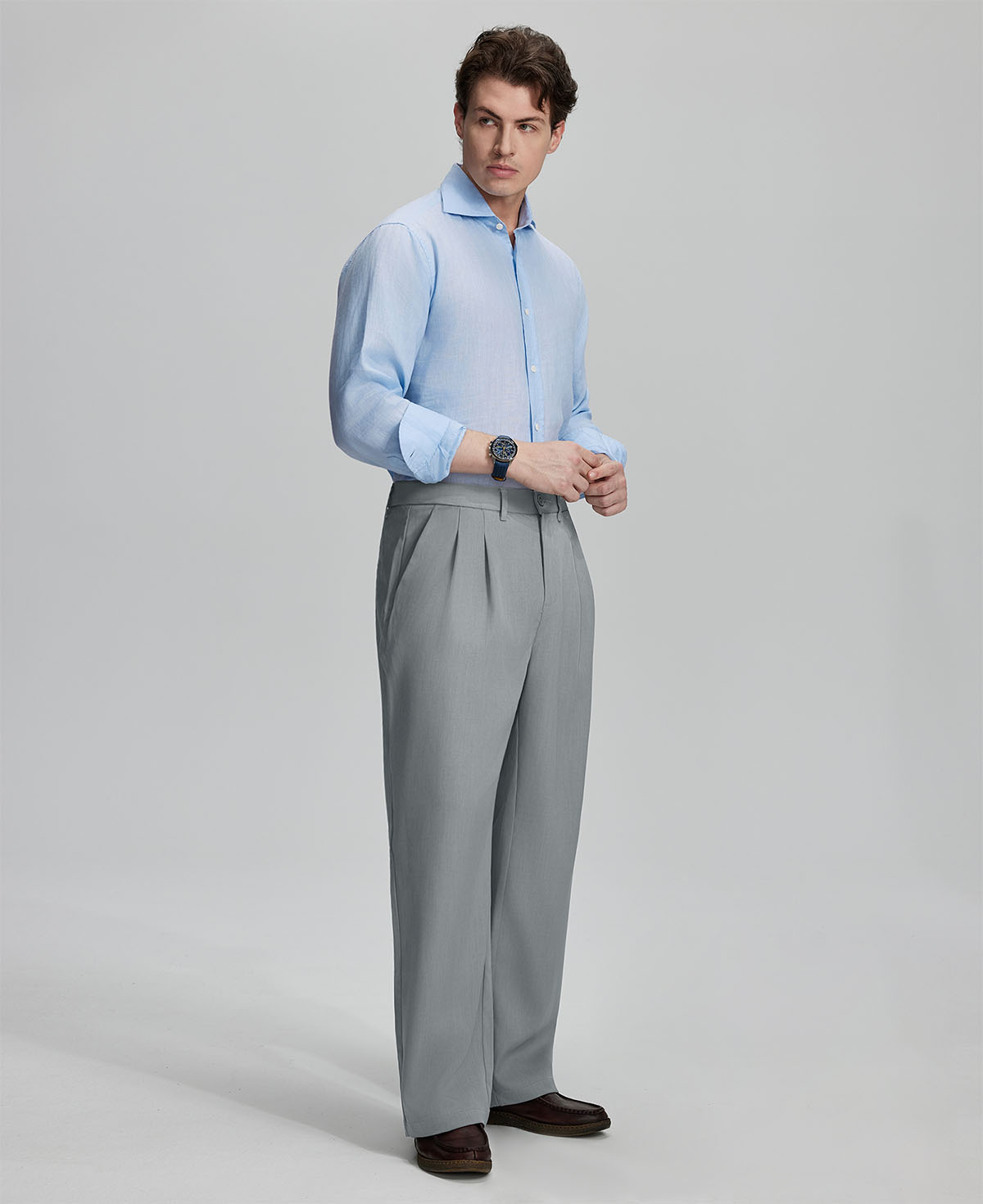 Side view of man adjusting cuff while highlighting the clean lines and casual elegance of light grey pleated baggy dress pants.