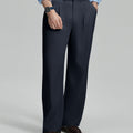 Man in light blue shirt, navy pleated pants, and brown shoes, hand in pocket showcasing relaxed fit and drape.