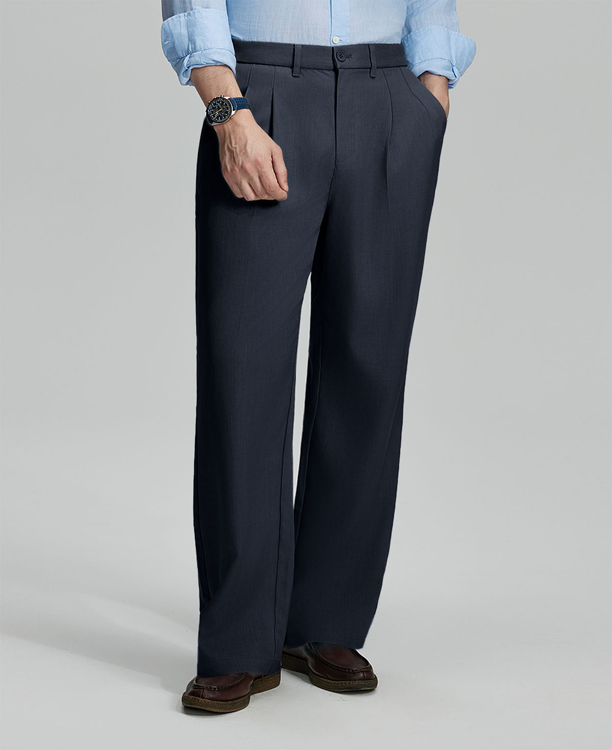 Man in light blue shirt, navy pleated pants, and brown shoes, hand in pocket showcasing relaxed fit and drape.