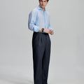 Side view of man adjusting cuff while highlighting the clean lines and casual elegance of navy pleated baggy dress pants.