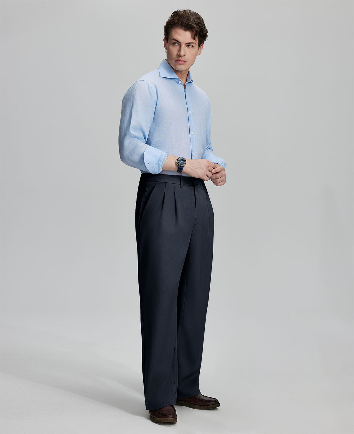 Side view of man adjusting cuff while highlighting the clean lines and casual elegance of navy pleated baggy dress pants.
