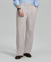 Man in light blue shirt, stone grey pleated pants, and brown shoes, hand in pocket showcasing relaxed fit and drape.