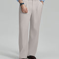 Man in light blue shirt, stone grey pleated pants, and brown shoes, hand in pocket showcasing relaxed fit and drape.
