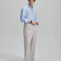 Side view of man adjusting cuff while highlighting the clean lines and casual elegance of stone grey pleated baggy dress pants.