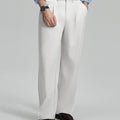 Man in light blue shirt, white pleated pants, and brown shoes, hand in pocket showcasing relaxed fit and drape.