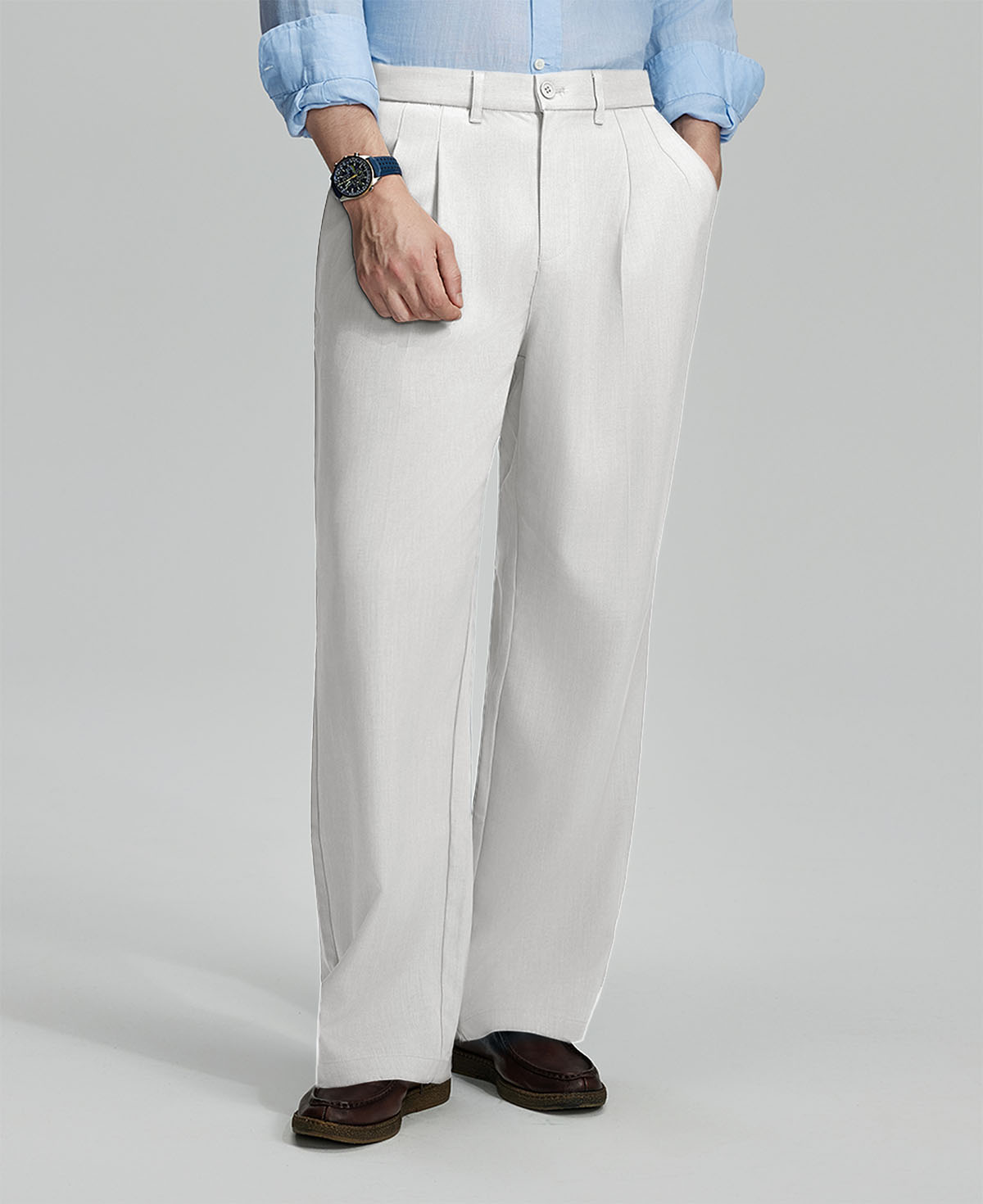 Man in light blue shirt, white pleated pants, and brown shoes, hand in pocket showcasing relaxed fit and drape.