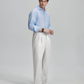 Side view of man adjusting cuff while highlighting the clean lines and casual elegance of white pleated baggy dress pants.