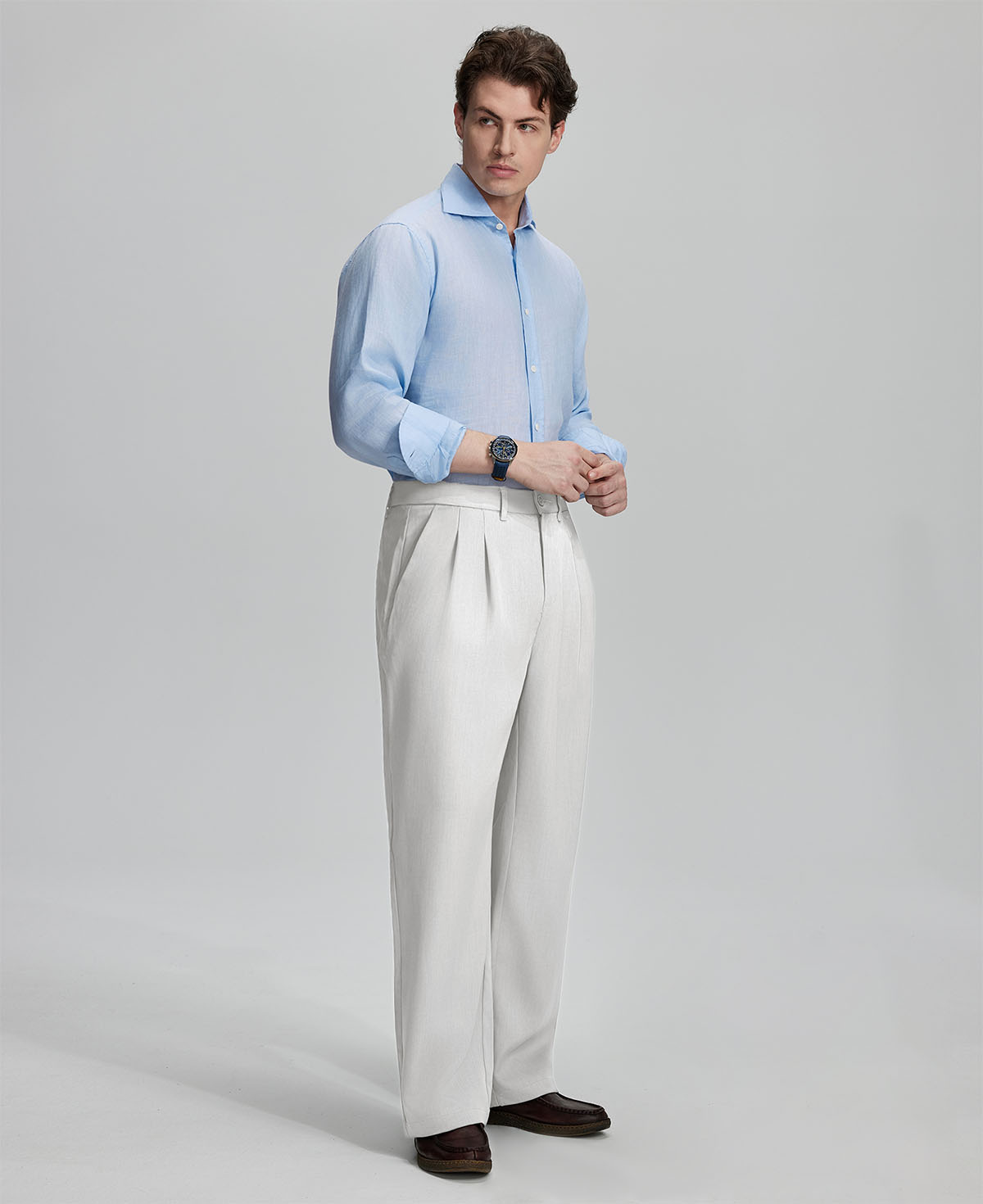Side view of man adjusting cuff while highlighting the clean lines and casual elegance of white pleated baggy dress pants.