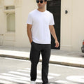 Man wearing white tee and black durable multipants standing on a street, hand in pocket, showcasing daily wear.