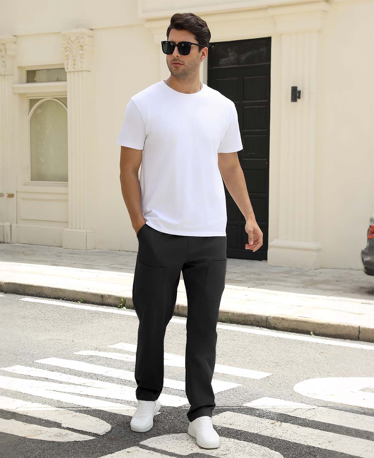 Man wearing white tee and black durable multipants standing on a street, hand in pocket, showcasing daily wear.