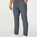 Man in dark grey multipants with drawstring waist and multiple pockets, white sneakers, hand in pocket showing side logo.