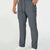 Man in dark grey multipants with drawstring waist and multiple pockets, white sneakers, hand in pocket showing side logo.