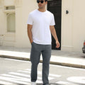 Man wearing white tee and dark grey durable multipants standing on a street, hand in pocket, showcasing daily wear.