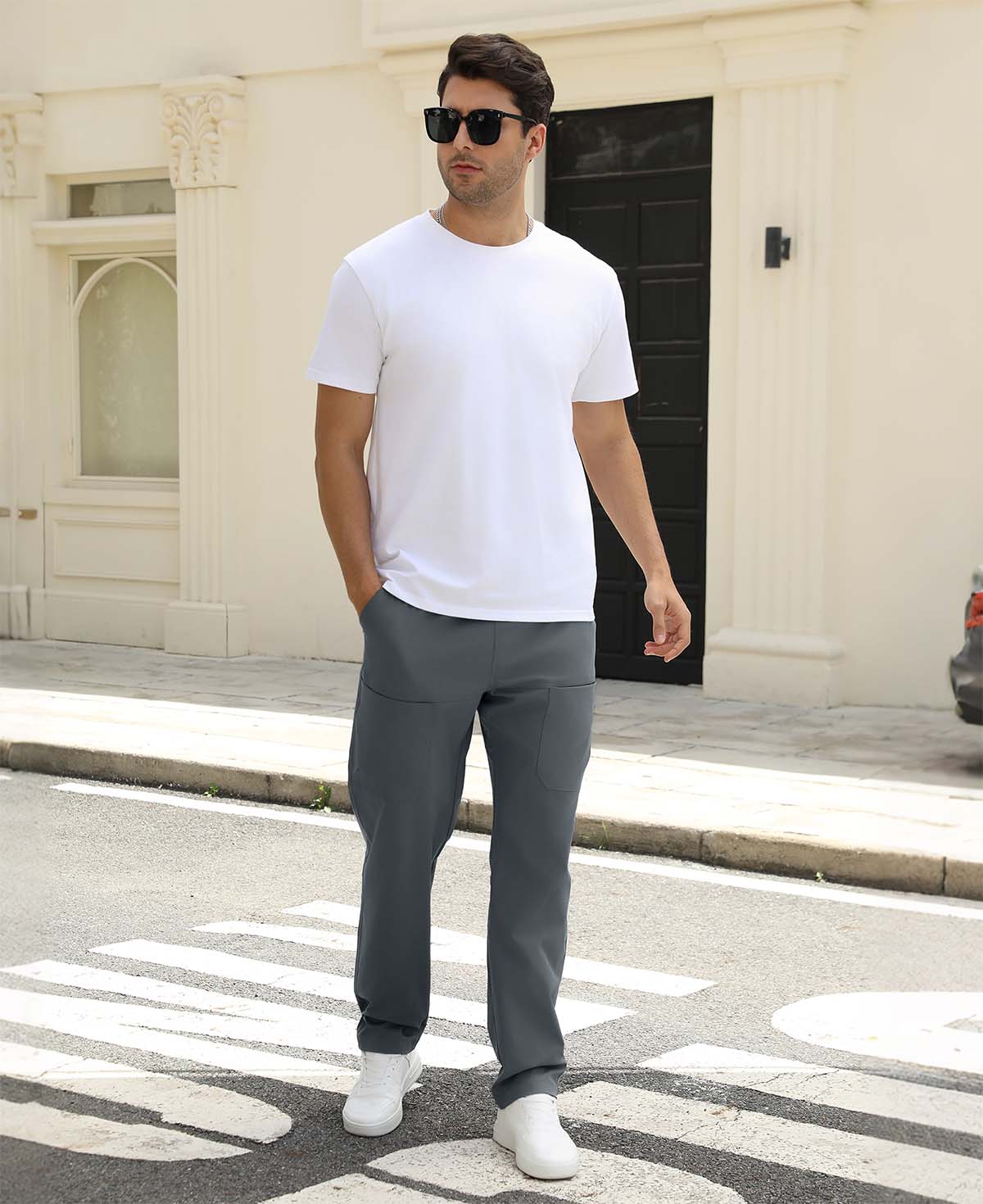Man wearing white tee and dark grey durable multipants standing on a street, hand in pocket, showcasing daily wear.