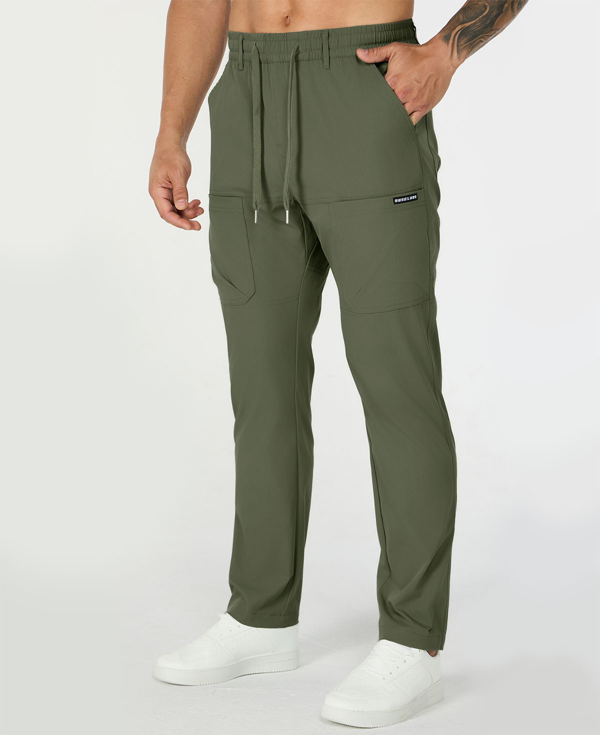 Man in green multipants with drawstring waist and multiple pockets, white sneakers, hand in pocket showing side logo.