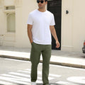 Man wearing white tee and green durable multipants standing on a street, hand in pocket, showcasing daily wear.