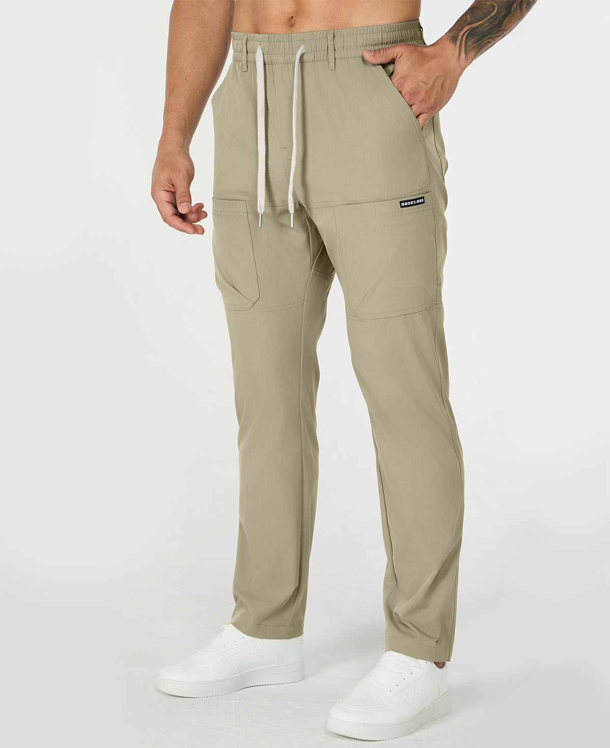 Man in khaki multipants with drawstring waist and multiple pockets, white sneakers, hand in pocket showing side logo.
