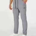 Man in light grey multipants with drawstring waist and multiple pockets, white sneakers, hand in pocket showing side logo.