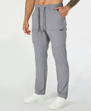 Man in light grey multipants with drawstring waist and multiple pockets, white sneakers, hand in pocket showing side logo.