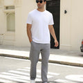 Man wearing white tee and light grey durable multipants standing on a street, hand in pocket, showcasing daily wear.